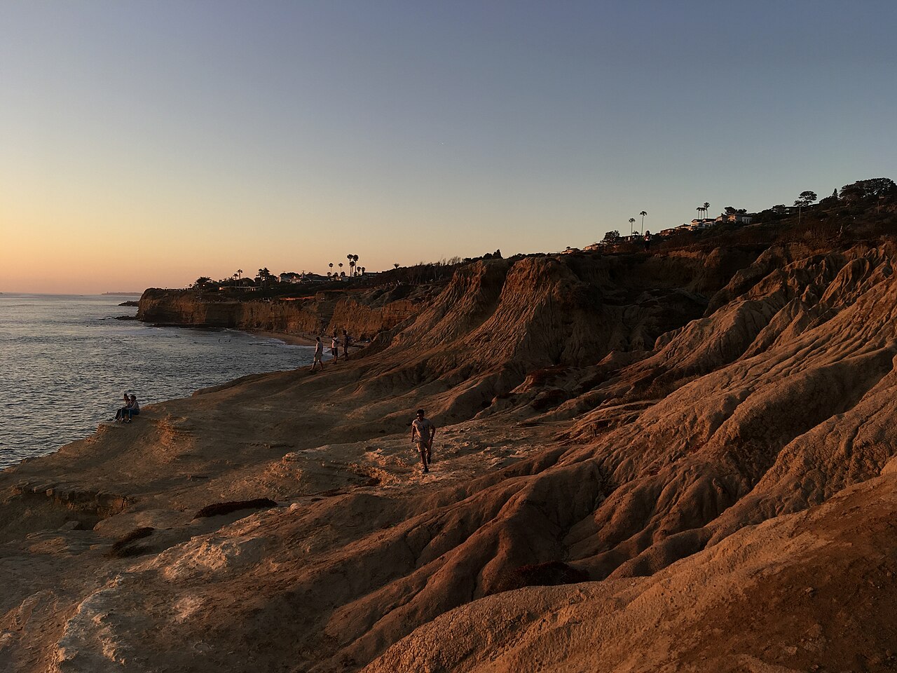 Layered sandstone shelves at Sunset Cliffs, with people on the rock and the ocean to the left.